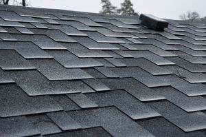 Gray asphalt shingle roof with a small roof vent and cloudy sky in the background