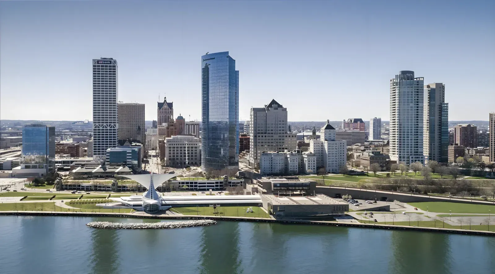 Riverfront city skyline with modern high-rises and a monument along the waterfront under a clear sky