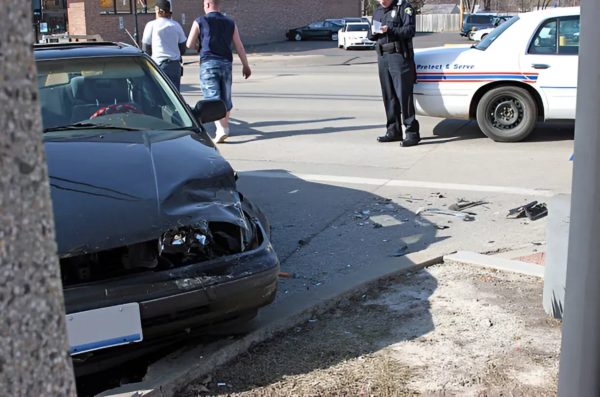 Damaged car at roadside accident scene with police and pedestrians nearby