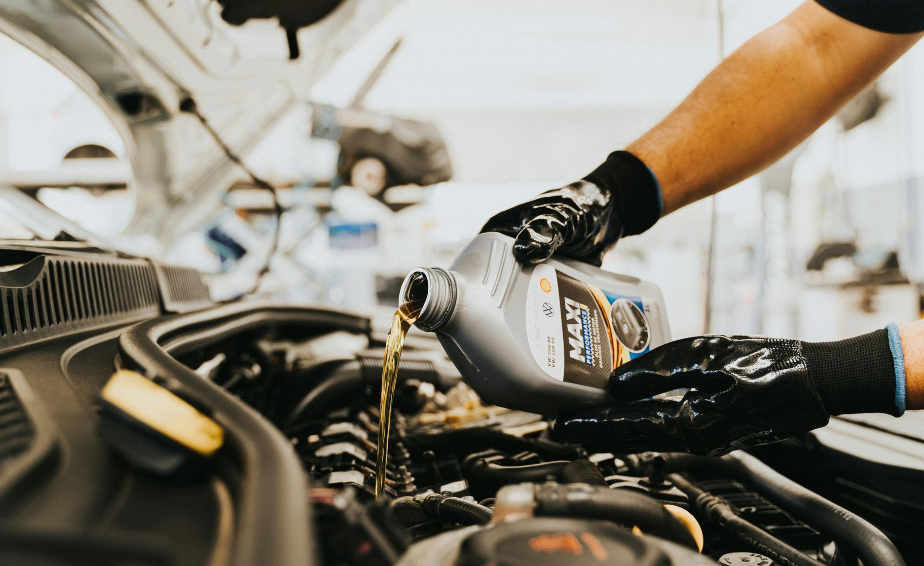 A mechanic in black gloves pours new motor oil into a car engine at an auto repair shop.