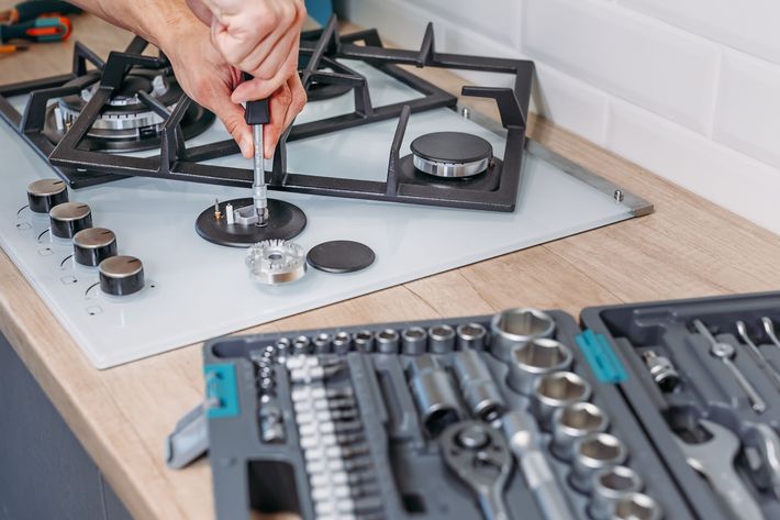A person is fixing a gas stove with a screwdriver.