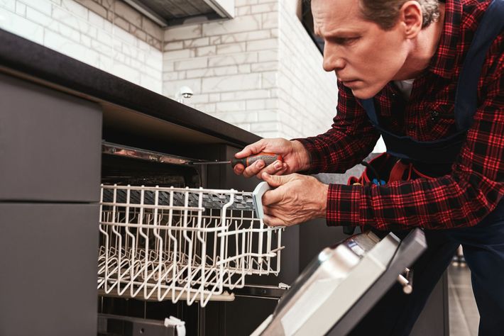 Man repairing a dishwasher with the open rack pulled out and tools in hand
