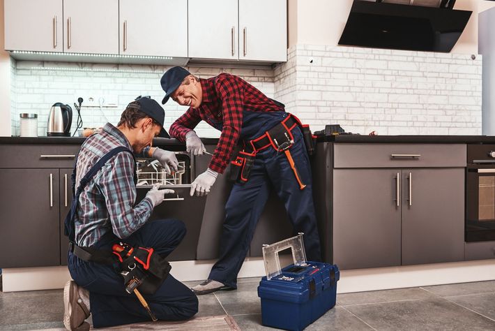 Two plumbers repairing a kitchen oven, with tools on the floor and a blue toolbox nearby in Chicago Tiger Appliance Repair.