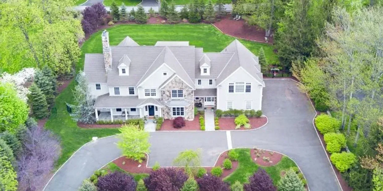 An aerial view of a large house with a large driveway surrounded by trees.