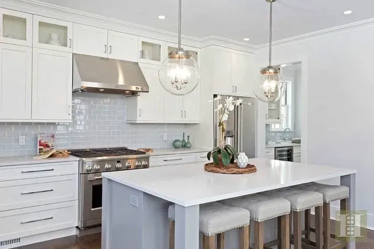 A kitchen with white cabinets , stainless steel appliances , and a large island.