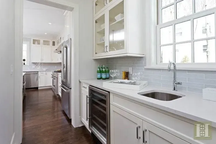 A kitchen with white cabinets , stainless steel appliances , a sink and a refrigerator.