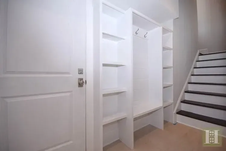 A hallway with stairs and a closet with shelves and hooks.