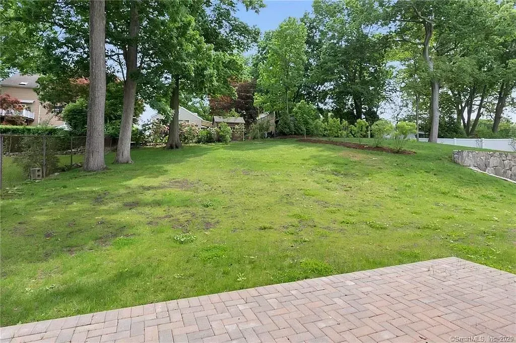 A large lawn with trees in the background and a brick driveway