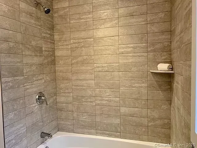 A bathroom with a tub , shower , and tiled walls.