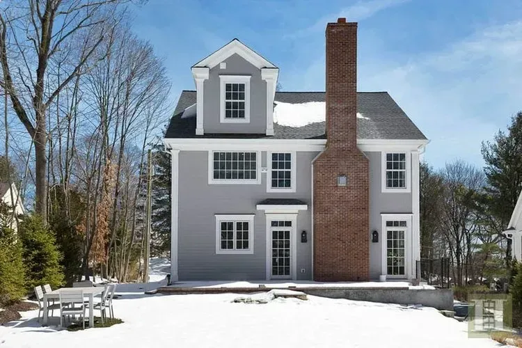 A large house with a brick chimney is surrounded by snow