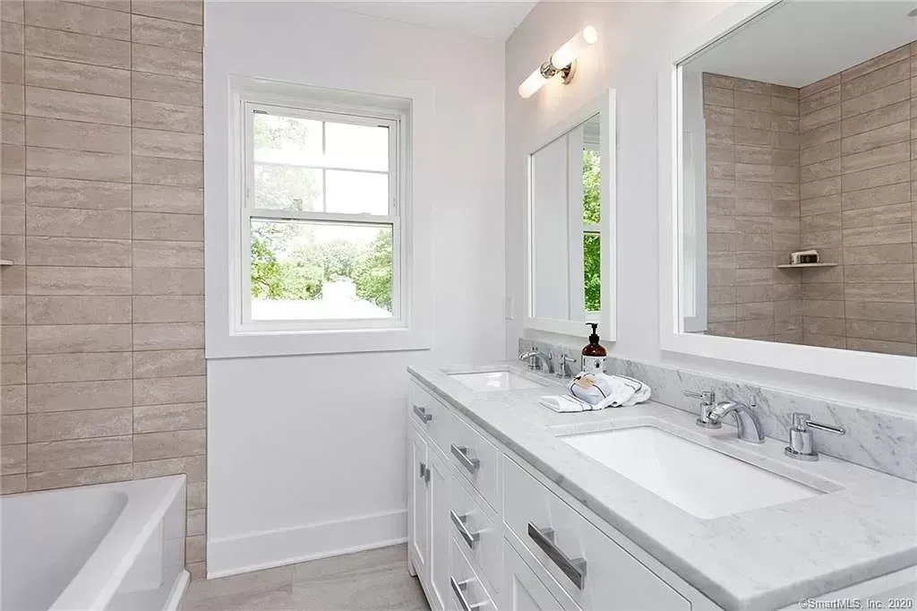A bathroom with two sinks , a tub and a window.