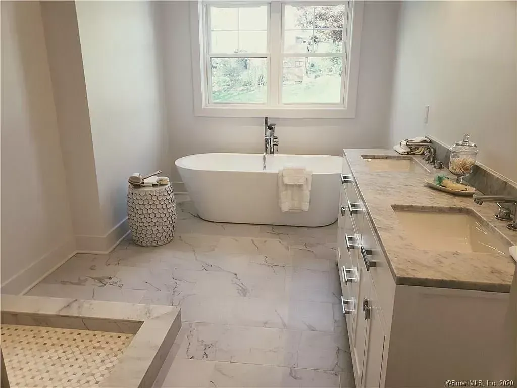 A bathroom with a tub , sinks , and a window.