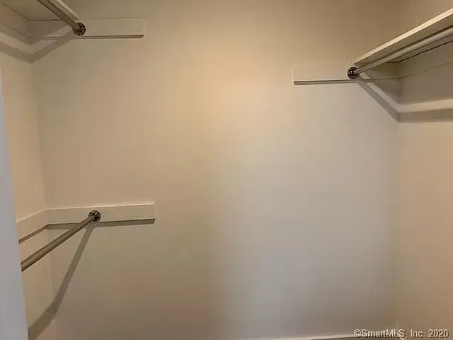 An empty walk in closet with a white wall and shelves.