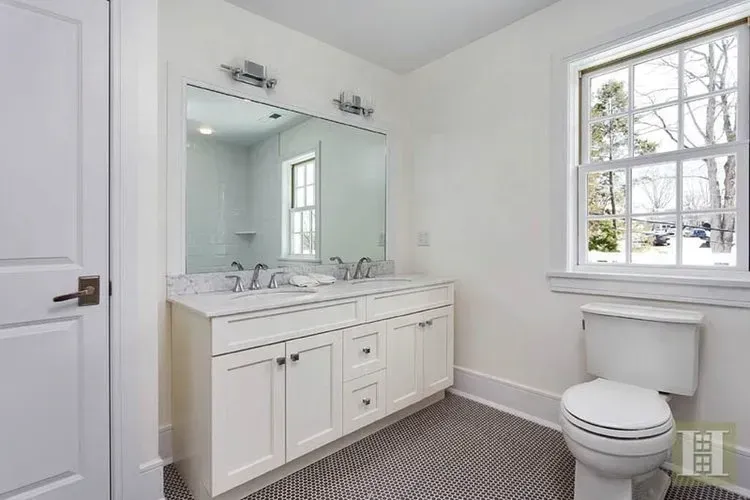 A bathroom with a toilet , sink , mirror and window.