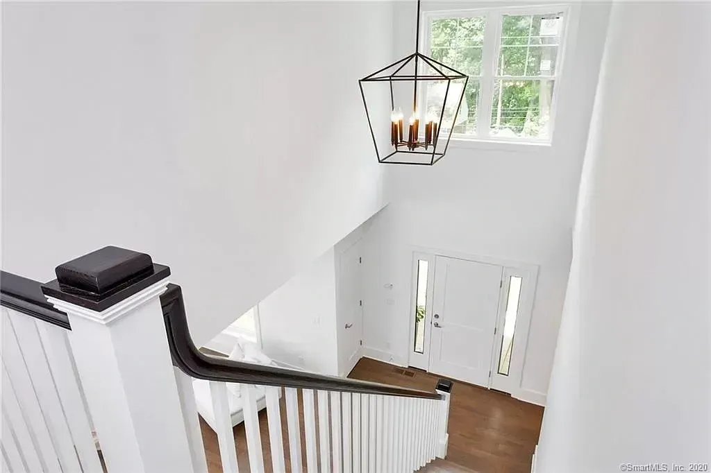 A white staircase with a black railing and a chandelier hanging from the ceiling.