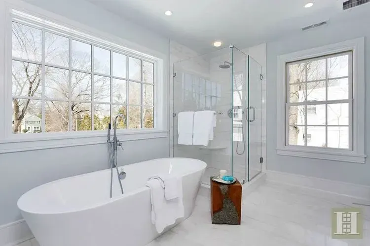 A bathroom with a tub , shower and two windows.