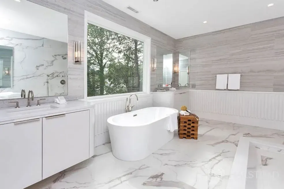 A bathroom with a tub , sink , mirror and window.