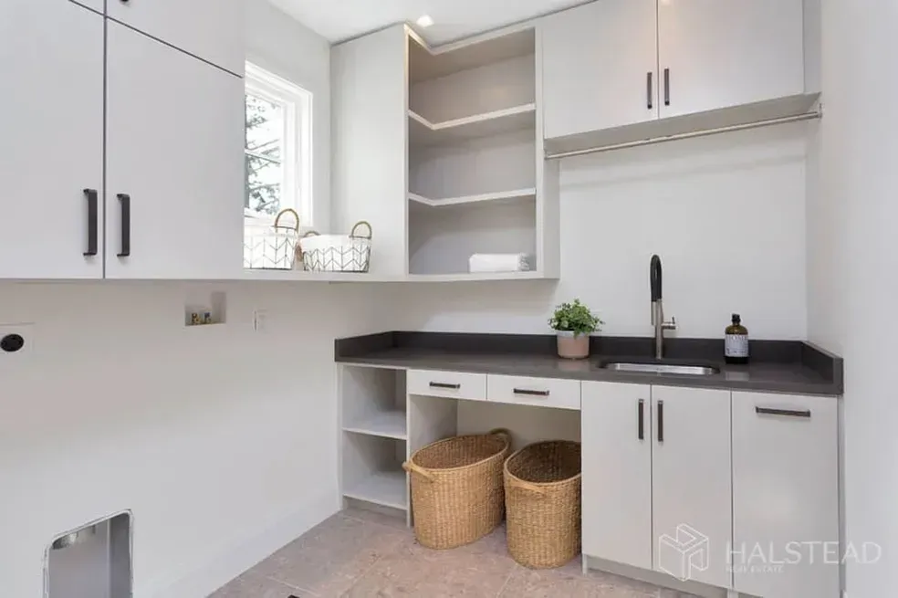 A laundry room with white cabinets , a sink , and wicker baskets.