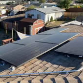 Solar panels installed on a shingle rooftop in a suburban neighborhood, with a small shed nearby.