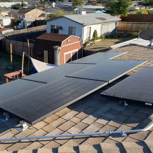 Solar panels installed on a shingle rooftop in a suburban neighborhood, with a small shed nearby.