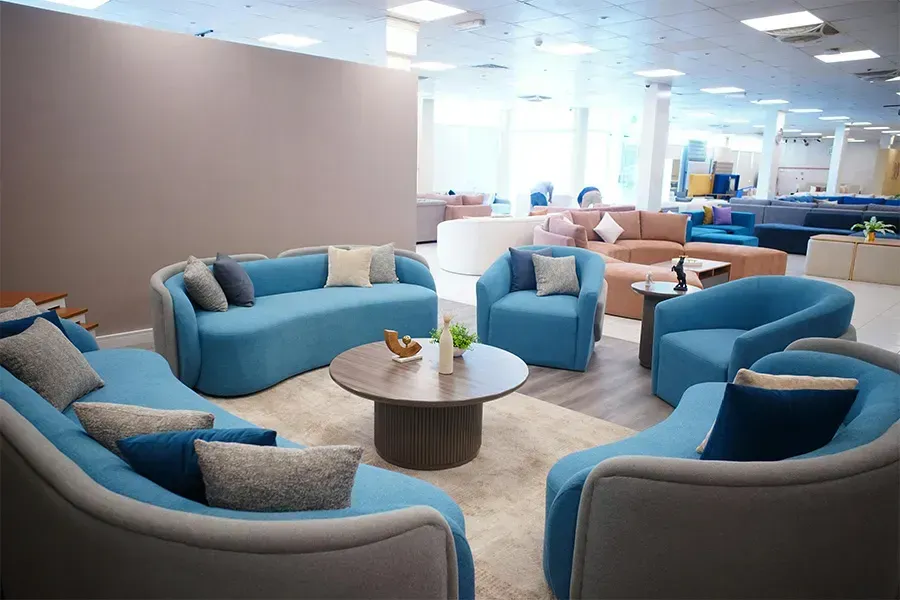 Modern office lounge with blue and tan sofas around a round table in a bright open workspace