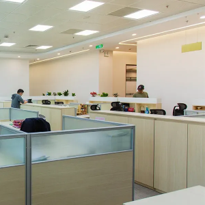 Open-plan office with desks, cubicles, and a few people working under bright ceiling lights