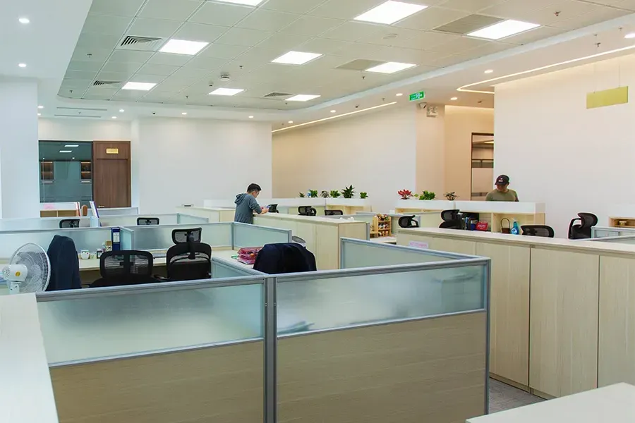 Modern office reception area with desks, cubicles, and a few people working under bright ceiling lights