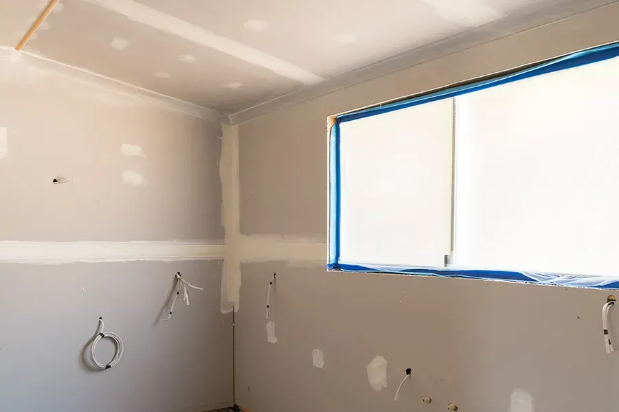Unfinished drywall room with taped seams, a blue-taped window, and exposed wiring.