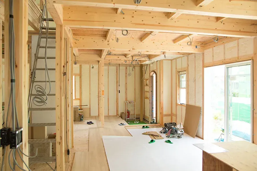 Interior of a house under construction with exposed wood framing and tools on the floor.