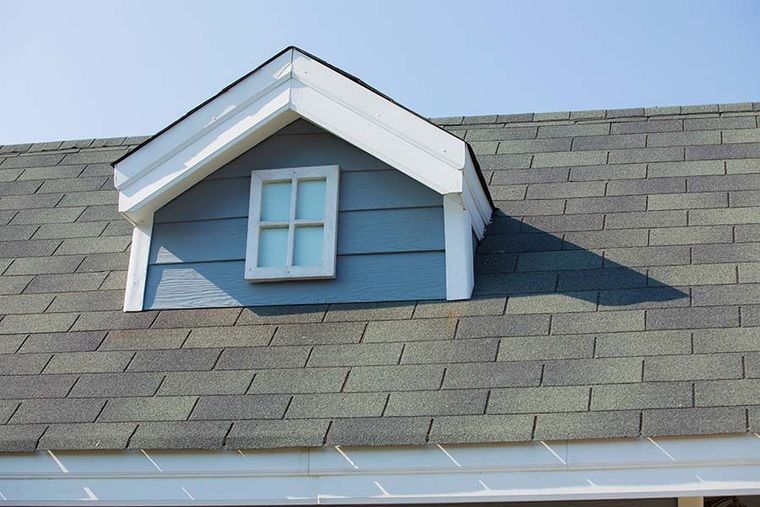 Blue dormer window on a gray shingled roof under a clear sky