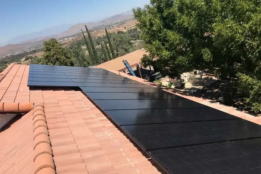 Solar panels installed on a house roof under a clear blue sky, with trees in the background
