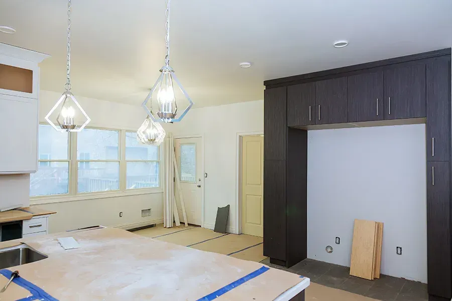 Modern kitchen under renovation with dark cabinets, white walls, hanging lights, and covered island.