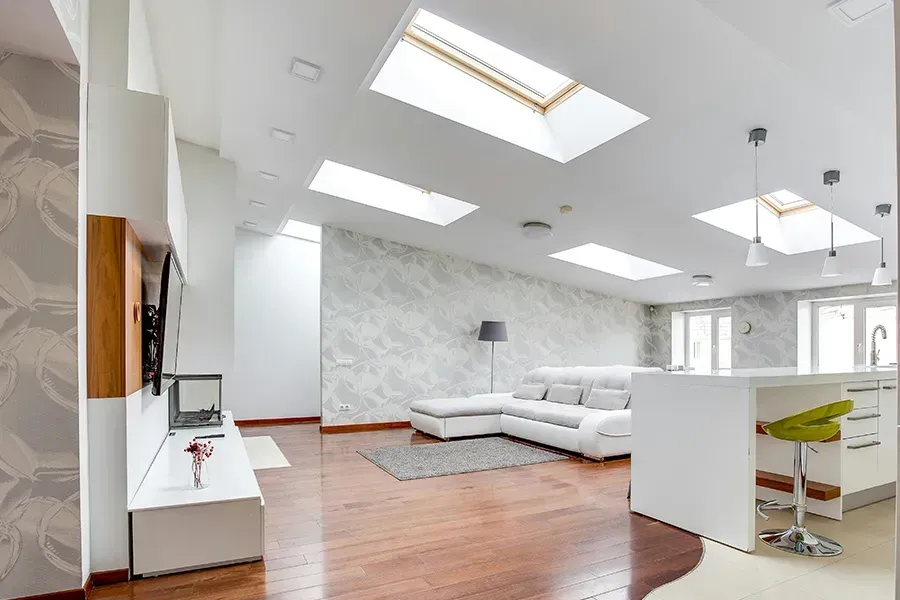 Bright modern living room with white sectional sofa, skylights, wood floors, and open kitchen area.