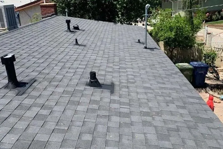 Gray shingled roof with several black vent pipes and a chimney on a residential house