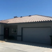 Single-story stucco house with a tiled roof, two-car garage, and palm tree in front.