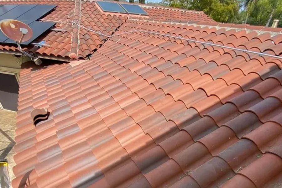 Red tiled roof with solar panel and skylights under bright sunlight.