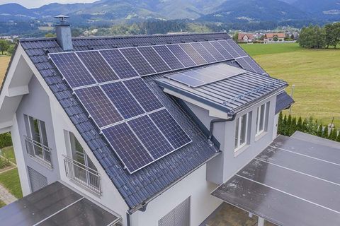 House with solar panels on a gray roof overlooking green fields and mountains
