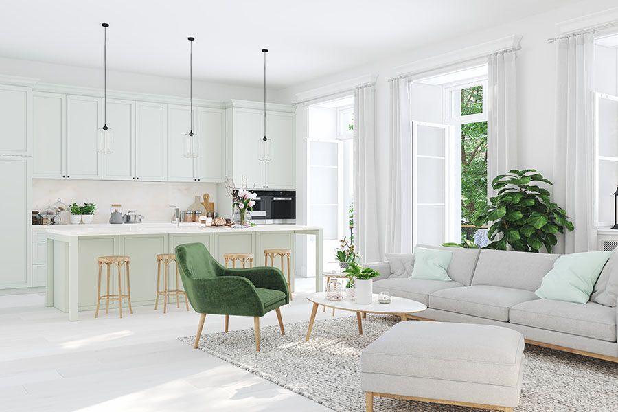 Bright white living room with green chair, gray sofa, and open kitchen in the background
