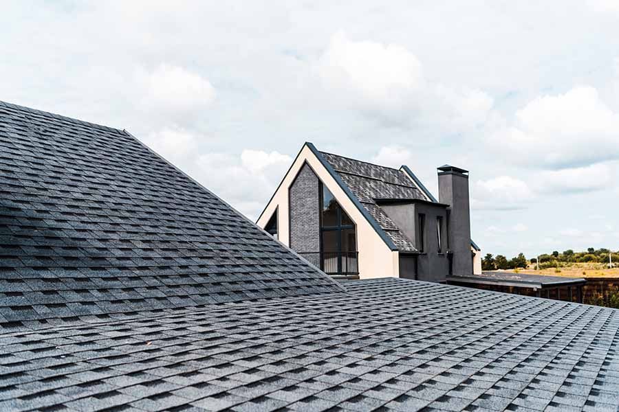 Gray shingled rooftops with a modern house and chimney under a cloudy sky