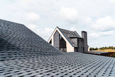 Slate roof in foreground with a modern house and cloudy sky in the background