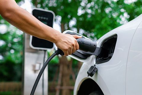 Person plugging a charging cable into a white electric car at a charging station