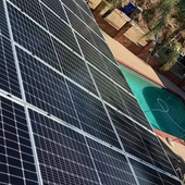 Solar panels installed on a roof beside a turquoise swimming pool and patio area