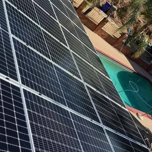 Solar panels installed on a roof beside a turquoise swimming pool and patio area