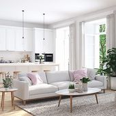Bright white living room with sectional sofa, coffee table, kitchen, and large windows with sheer curtains