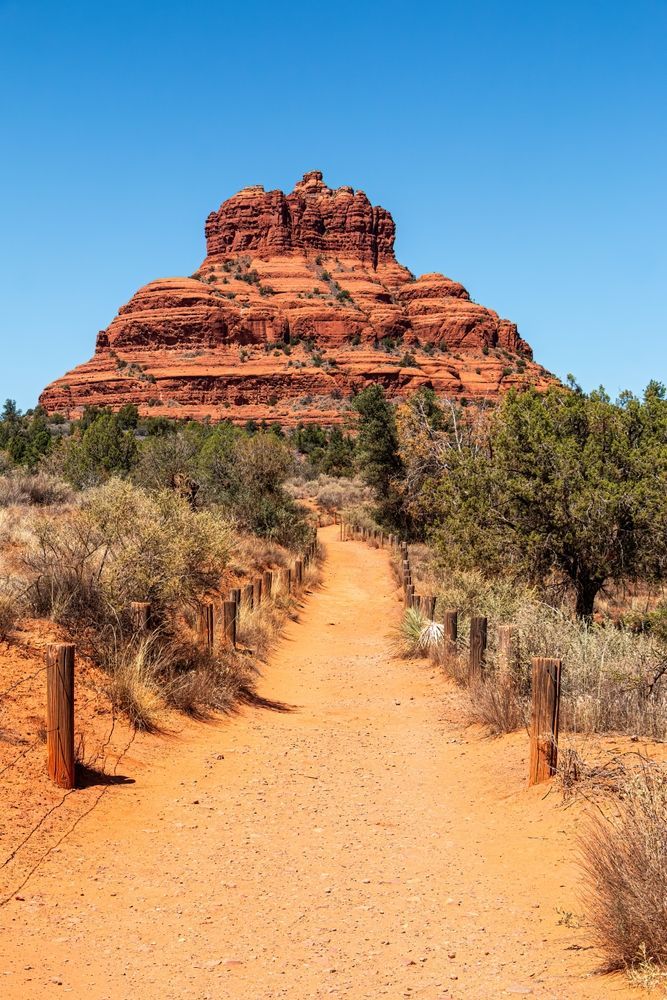 Red sandstone butte beyond a sandy trail under a clear blue sky