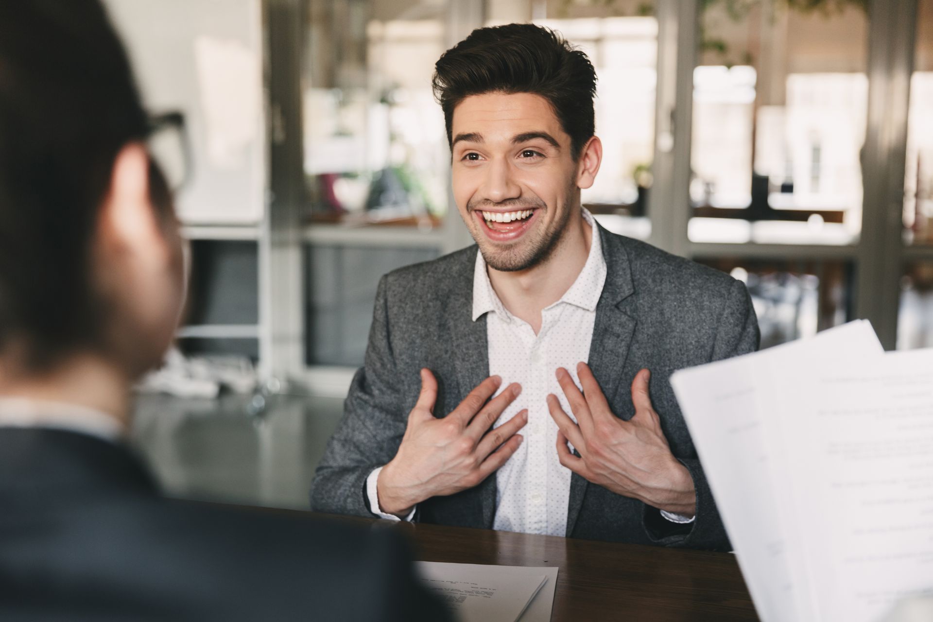 The young man is smiling, with both hands against his chest, referecing to himself in conversation. He now knows How Marijuana Pardons Affect Employee Background Checks