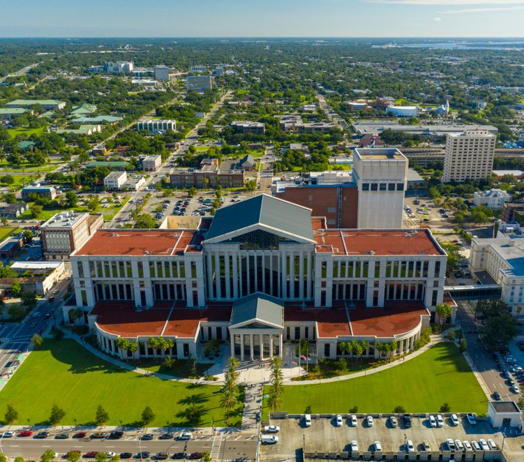 Aerial view of a large red-brick building with a central tower, surrounded by lawns and parking lots.
