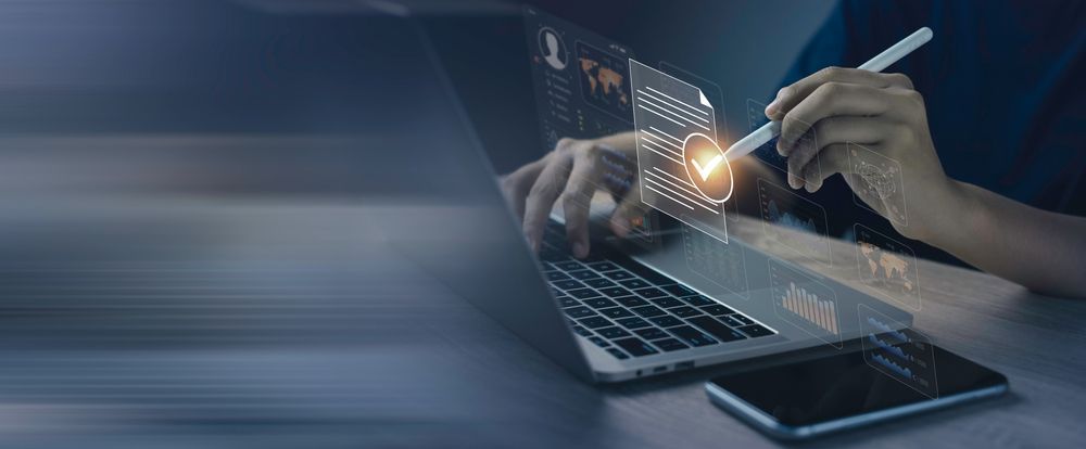 A person using a stylus on a digital interface above a laptop keyboard to select a glowing checkmark icon.