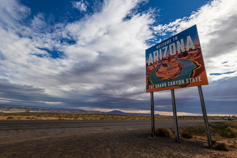 Arizona roadside sign against a cloudy sky and desert landscape