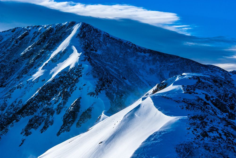 Snow-covered mountain ridge under a blue sky with wispy clouds
